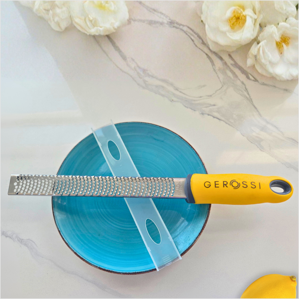 Stainless steel citrus zester grater beside fresh citrus, used for adding organic lemon or lime zest to low-sodium meals.