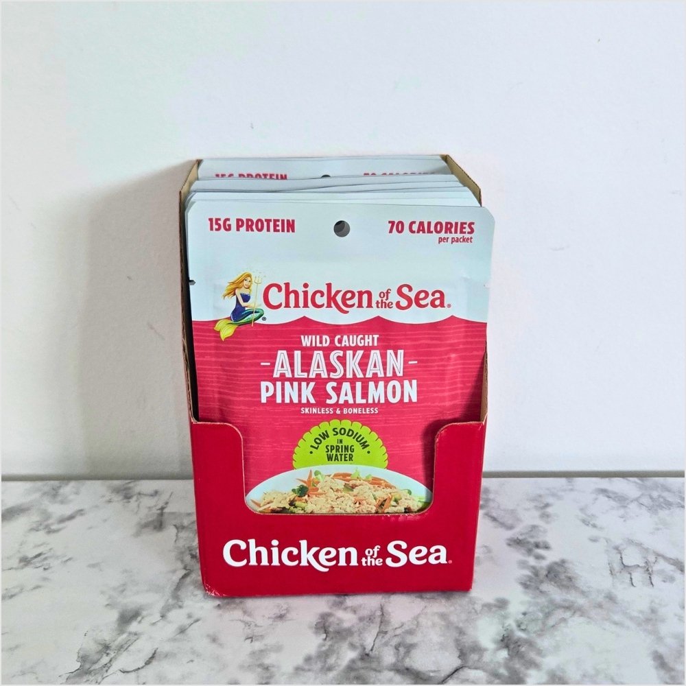 Chicken of the Sea low sodium wild caught Alaskan pink salmon pouches, standing in their open red display box on a kitchen counter.