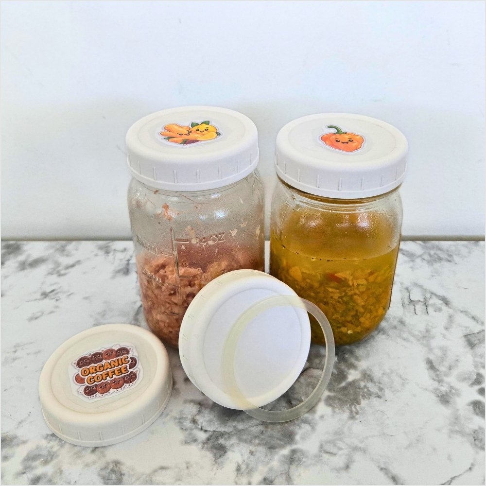 Two glass mason jars with white AOZITA regular mouth lids and handmade labels, pickled ginger on the left and pickled habaneros on the right, with two more lids on a marble counter.